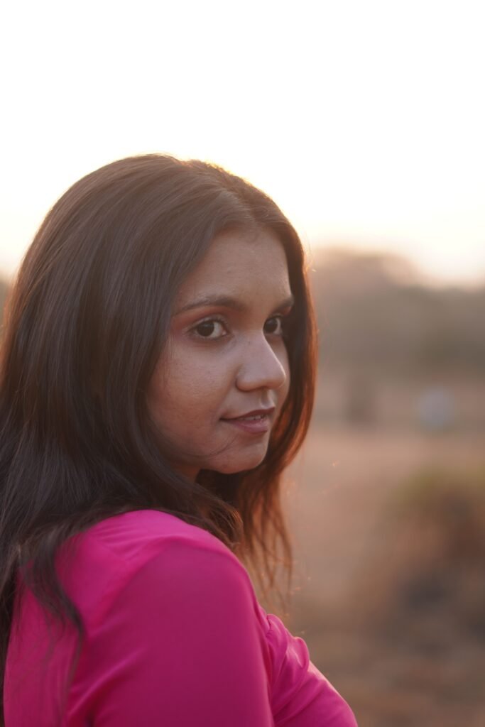 Portrait of a young woman in a pink top gazing at the camera with a serene background of a sunset outdoors.